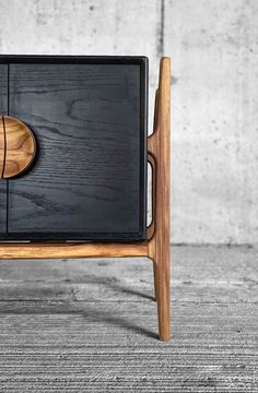 a black and wood sideboard with a wooden knob on it's top, sitting in front of a concrete wall