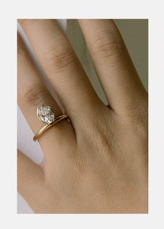 a woman's hand with a diamond ring on top of her finger, wearing a yellow gold band