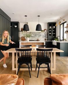 a woman sitting at a table in a kitchen with black cabinets and wooden flooring