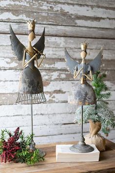 two metal angel figurines sitting on top of a wooden table next to christmas decorations