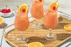 three glasses filled with orange juice and garnished with cherries on a tray