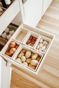 an open drawer in a kitchen filled with different types of potatoes and onions on the floor