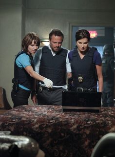 three people standing around a table with a laptop computer on it and one person wearing gloves