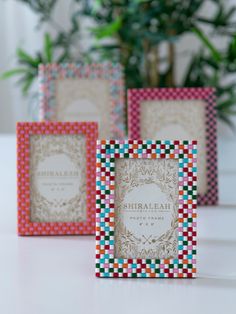 three small colorful frames sitting next to each other on a white counter top with a potted plant in the background