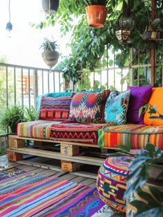 an outdoor seating area with colorful pillows and rugs on the floor, surrounded by potted plants