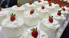 a table topped with lots of white cakes covered in frosting and strawberries next to each other