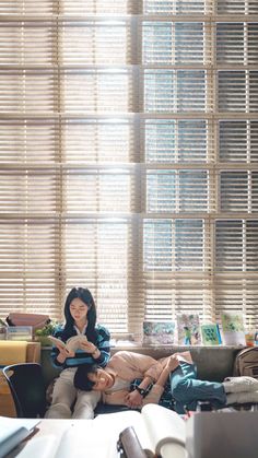 a woman sitting on top of a couch in front of a window holding a book