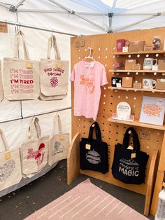 two totes are hanging on the wall in front of a display with t - shirts