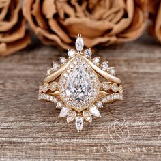 an engagement ring with a pear shaped diamond surrounded by smaller round brilliant cut diamonds on a wooden surface