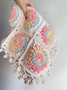 a hand is holding a crocheted pillow with tassels