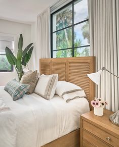 a bed with white sheets and pillows in front of a window next to a wooden dresser