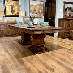 a dining room table with tea cups on it in front of wooden dressers and framed pictures