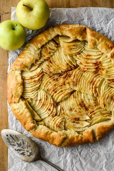 an apple pie with sliced apples next to it on top of a piece of wax paper