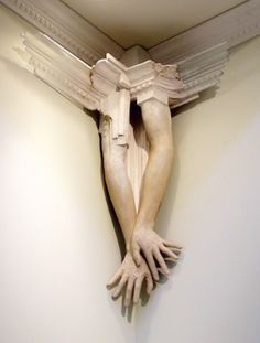 a white statue with hands on it's face and arms hanging from the ceiling