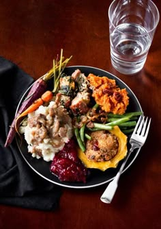 a plate with meat, mashed potatoes and veggies next to a glass of water