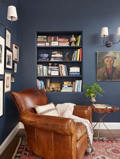 a living room with blue walls and leather chair in front of a book shelf filled with books