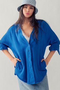 Bold blue buttondown, slightly oversized, and made of airy gauze material. Perfect as a cover-up or for a casual look. The In The Blue Buttondown adds a touch of playfulness to any outfit! Relaxed Blue Tops For Daywear, Casual Cotton Gauze Tops For Vacation, Relaxed Blue Tops With Pockets, Trendy Blue Top With Roll-up Sleeves, Blue Cotton Summer Cover-up, Oversized Denim Blue Button-up Top, Oversized Blue Button-up Blouse, Washed Blue Button-up Top With Frayed Hem, Blue Button-up Sleepwear With Button Closure