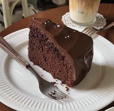 a piece of chocolate cake on a plate with a fork and cup of coffee in the background