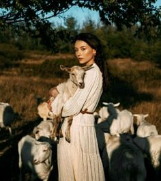 a woman holding a lamb in front of a herd of sheep