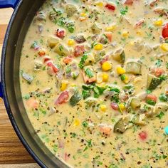 a blue pan filled with soup and vegetables on top of a wooden table next to a spoon