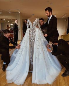 two men are working on a wedding dress in the middle of a room with other people