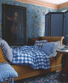 a bed with blue and white sheets in a bedroom next to a painting on the wall