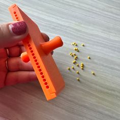 a hand holding an orange plastic object with holes in it and tiny yellow beads on the table