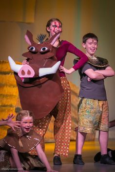 two children and an adult are on stage with a cow costume in front of them