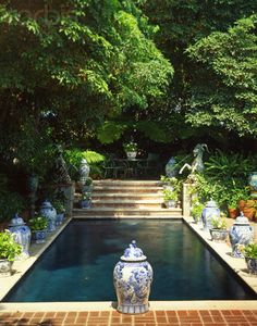 an outdoor pool surrounded by trees and potted plants in the foreground, with steps leading up to it