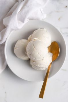 two scoops of ice cream on a white plate with a gold spoon next to it