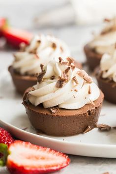 chocolate cupcakes topped with whipped cream and strawberries on a white platter