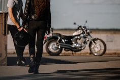 a man and woman walking down the street with their motorcycle in the backround