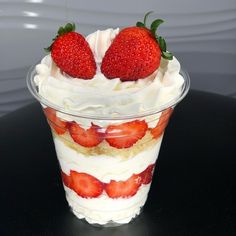 two strawberries on top of whipped cream in a plastic cup sitting on a table