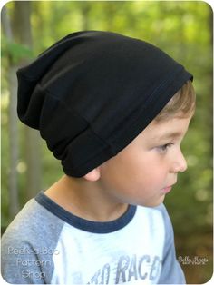 a young boy wearing a black beanie in the woods, looking off into the distance