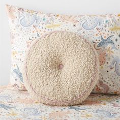 a round pillow sitting on top of a bed next to a pillow with an animal pattern