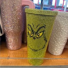 a green cup with yellow eyes sitting on top of a table next to other cups