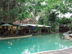 an outdoor swimming pool with tables and umbrellas next to the water in front of some trees