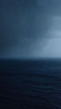 an airplane flying over the ocean on a cloudy day with dark clouds in the sky