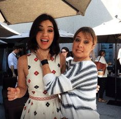 two women standing next to each other under an umbrella