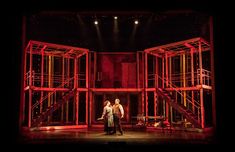 two people standing on stage in front of some red scaffoldings and lights