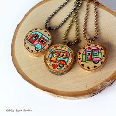 three necklaces with different designs on them sitting on a piece of wood next to a chain