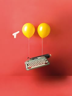 an old typewriter with two balloons attached to it's sides, sitting in front of a red wall