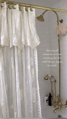 the shower curtain is white and has gold hardware on it, along with an antique faucet