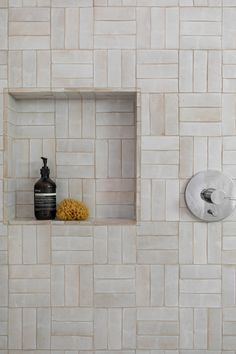 a bathroom with white tile and yellow flowers on the shelf next to the shower faucet