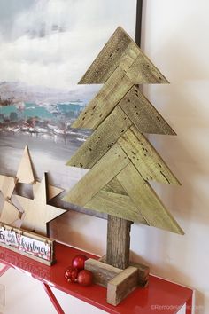 a wooden christmas tree sitting on top of a red shelf in front of a painting