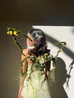 a woman standing in front of a white wall with yellow flowers on her head and arms