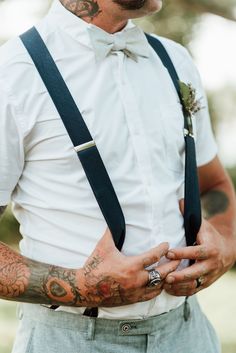 a man with tattoos wearing suspenders and a white shirt is holding his hand in his pocket