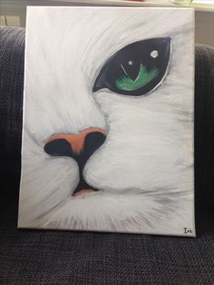 a painting of a white cat's face with green eyes on a gray couch