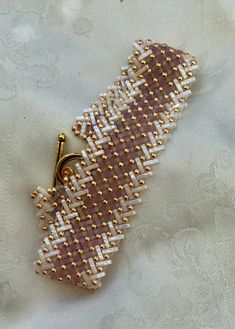 a piece of beaded fabric with a gold clasp on it's end, sitting on a white table cloth