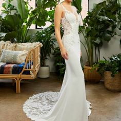 a woman in a white dress standing next to plants and potted plants on the floor